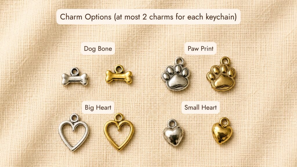 Customizable pet memorial keychain charm options displayed on cream linen fabric, including dog bone, paw print, heart outline, and small heart charms in silver and gold finishes.