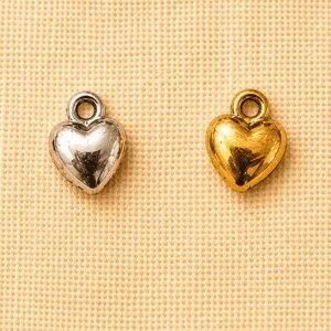 Silver and gold small heart memorial charm pendants displayed on a beige linen background, suitable for pet remembrance jewelry, keepsakes, and personalized memorial gifts.