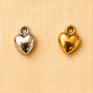 Silver and gold small heart memorial charm pendants displayed on a beige linen background, suitable for pet remembrance jewelry, keepsakes, and personalized memorial gifts.