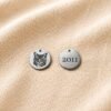 Front and back view of a personalized engraved pet charm on beige linen fabric, featuring a custom cat portrait on one side and the year “2011” engraved on the reverse side.
