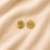 Front and back view of a personalized gold pet memorial charm displayed on cream linen fabric, featuring an engraved cat portrait and the message “Always loved Never forgotten.”